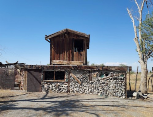 A rustic wooden structure with a stone base, set against a clear blue sky and sparse trees.