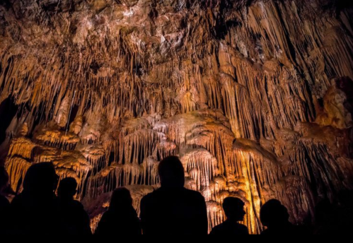 Silhouetted figures admire stunning stalactites and stalagmites in a dimly lit cave.