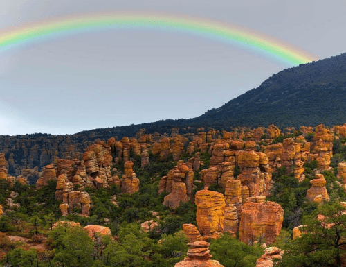 A vibrant rainbow arcs over a rugged landscape of towering rock formations and lush greenery.