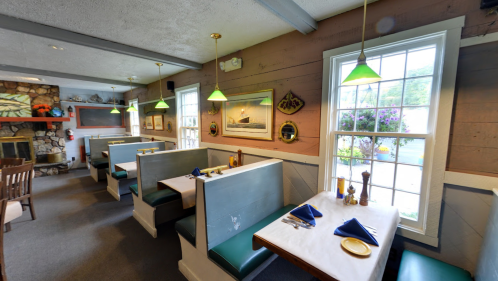 Cozy restaurant interior with booths, green pendant lights, and a stone fireplace, featuring a warm, inviting atmosphere.