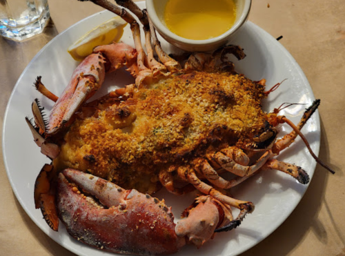 A plate of baked crab with a golden crust, served with melted butter and a lemon wedge.