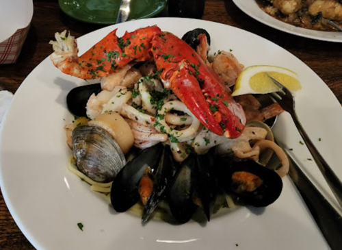 A seafood pasta dish featuring lobster, shrimp, clams, mussels, and squid, garnished with parsley and lemon.