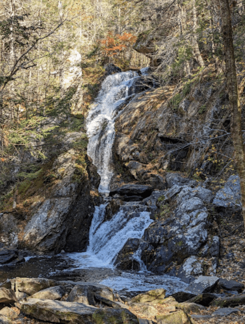 A serene waterfall cascading down rocky terrain, surrounded by trees and autumn foliage.
