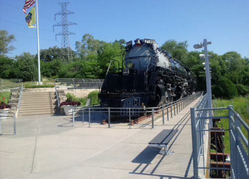 A vintage steam locomotive displayed on a platform surrounded by greenery and blue skies.