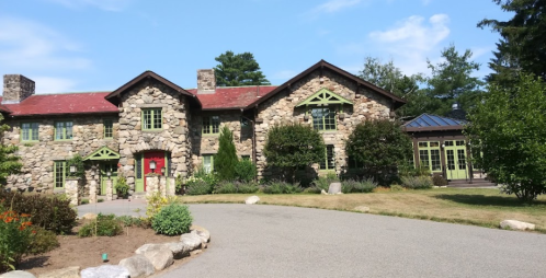 A large stone house with green accents, surrounded by trees and a landscaped garden on a sunny day.