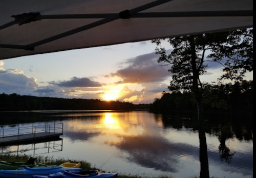 A serene lake at sunset, with colorful clouds reflecting on the water and kayaks lined up on the shore.