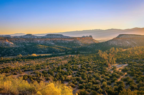 A scenic landscape featuring rolling hills, lush greenery, and a colorful sunset in the background.