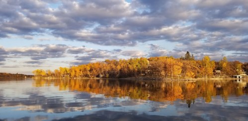 A serene lake scene with autumn trees reflecting on the water under a cloudy sky.