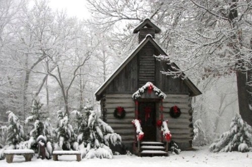 A cozy wooden cabin adorned with wreaths, surrounded by snow-covered trees in a winter landscape.
