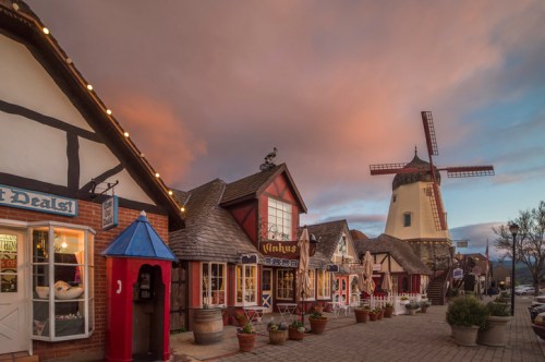 Charming village scene with quaint shops and a windmill under a colorful sky at dusk.