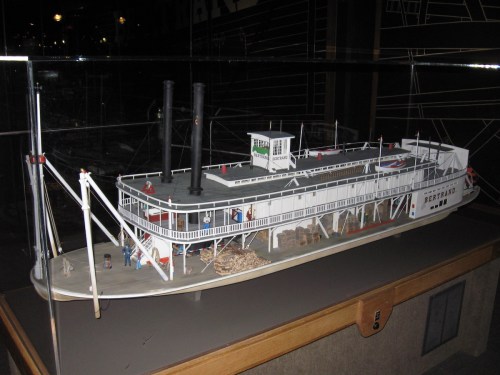 A detailed model of a steamboat with two smokestacks, displayed in a glass case.