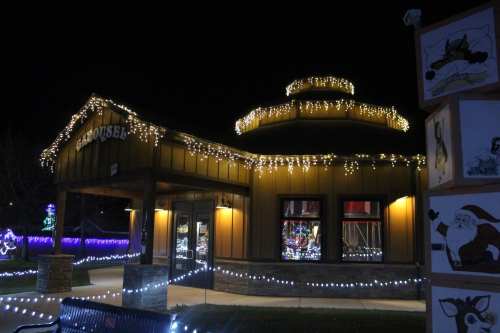 A festive building adorned with string lights, surrounded by holiday decorations at night.