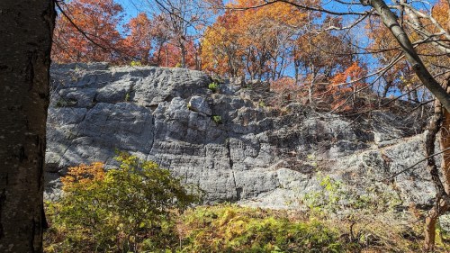 A rocky cliff surrounded by vibrant autumn foliage under a clear blue sky.