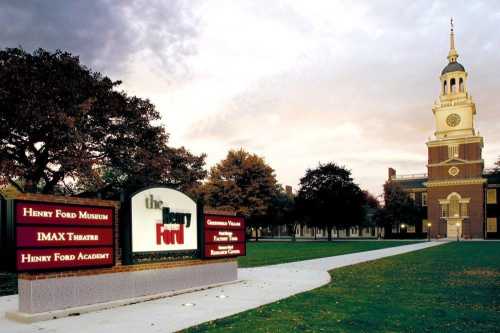 Sign for The Henry Ford, featuring the museum, IMAX Theatre, and Henry Ford Academy, with a building and trees in the background.