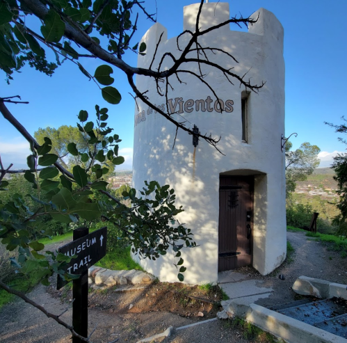 A white tower with a wooden door, labeled "Museo de las Ventas," surrounded by trees and a sign for a museum trail.