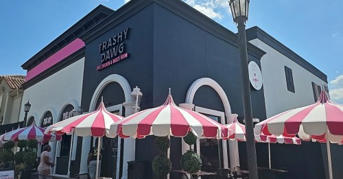 Exterior of a restaurant named "Trashy Diva," featuring red and white striped umbrellas and a bright blue sky.