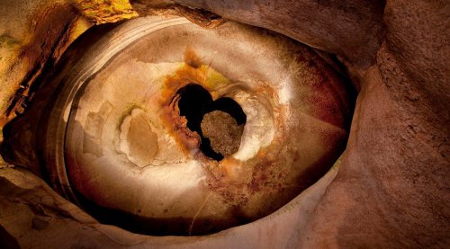 Aerial view of a circular rock formation with a heart-shaped opening, showcasing earthy tones and textures.