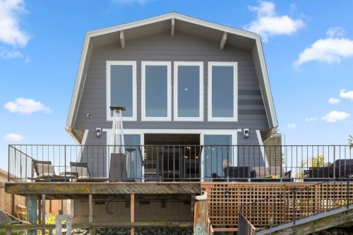 A modern gray house with large windows and a deck, set against a clear blue sky.