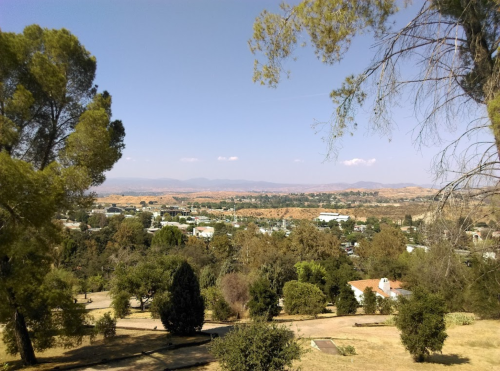 A scenic view of rolling hills and a small town under a clear blue sky, framed by trees in the foreground.