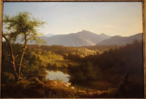 A serene landscape featuring mountains, a calm river, lush trees, and sheep grazing in a sunlit meadow.