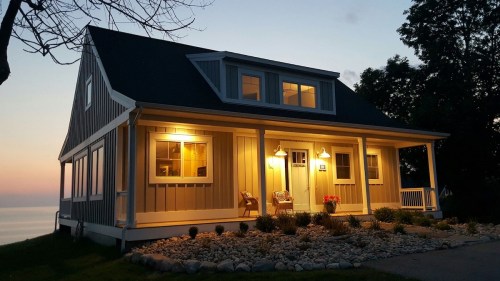 A cozy house with warm lights at dusk, surrounded by a landscaped yard and a view of the water in the background.
