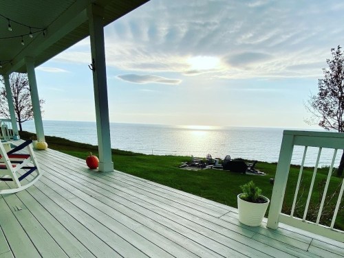 A serene view from a porch overlooking a calm lake at sunset, with chairs and a potted plant in the foreground.