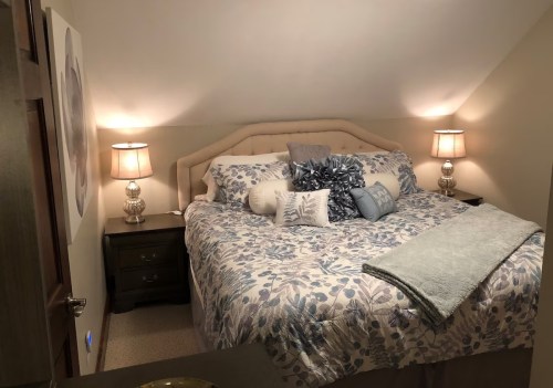 Cozy bedroom with a floral bedspread, decorative pillows, and soft lighting from two bedside lamps.