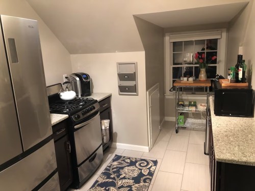 A cozy kitchen with stainless steel appliances, a window, and a small cart with plants and kitchen items.