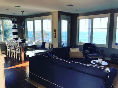 Bright, airy living space with a blue sofa, dining area, and large windows showcasing a view of the ocean.
