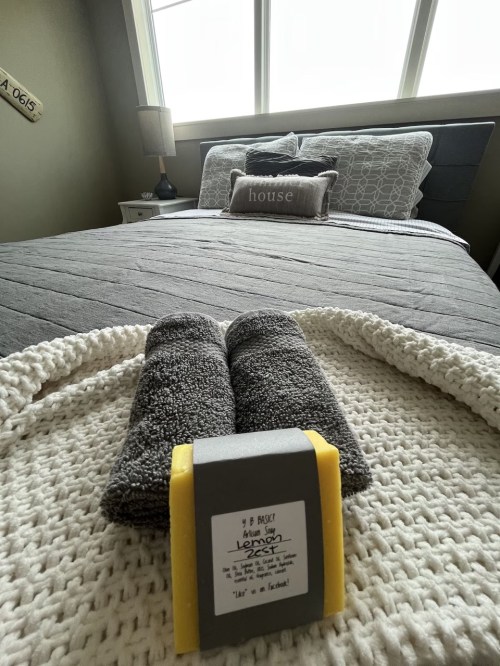 A cozy bedroom with a neatly made bed, a decorative pillow, and two rolled gray towels on a white blanket.