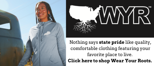 A smiling woman in a light blue shirt stands next to a vintage vehicle, promoting state pride clothing.