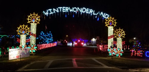 A brightly lit archway reading "WINTER WONDERLAND" with festive decorations, leading into a holiday light display at night.
