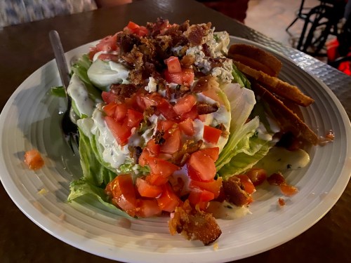 A fresh salad topped with diced tomatoes, bacon, and dressing, served with slices of bread on the side.