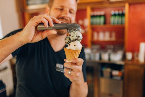 A man scoops ice cream into a cone at a shop, smiling as he adds a scoop of mint chocolate chip.
