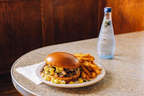A plate with a sandwich filled with meat and pineapple, served with fries and a bottle of sparkling water.