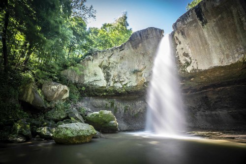 A serene waterfall cascading over a rocky cliff into a calm pool, surrounded by lush greenery.