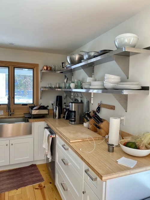 A modern kitchen with wooden countertops, open shelves, and various kitchenware, including bowls and a coffee maker.