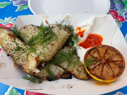 Crispy potato wedges topped with dill, served with a charred lemon and a side of creamy sauce and spicy dip.
