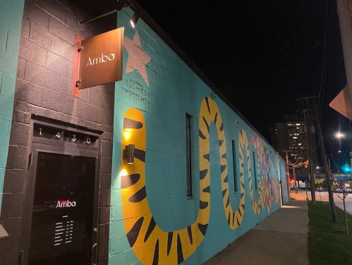 Exterior of Amba restaurant at night, featuring a colorful mural of a tiger on a blue wall.