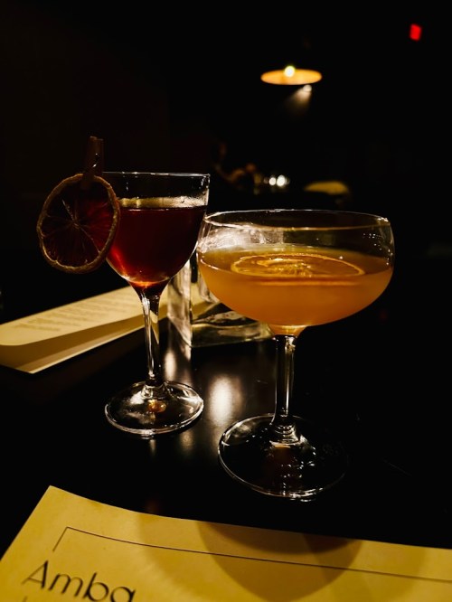 Two elegant cocktails on a dark table, one garnished with a dried lemon slice, the other with lemon wheels.