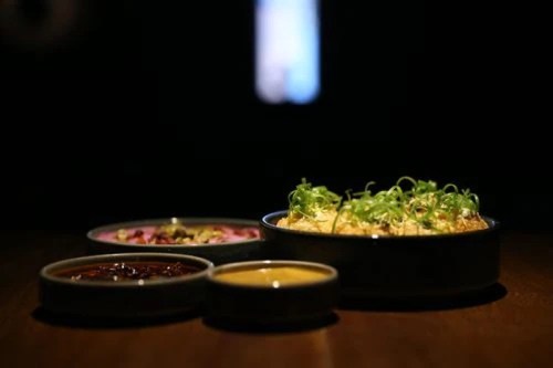 A dark setting featuring three bowls of colorful dishes, garnished with green onions, on a wooden table.