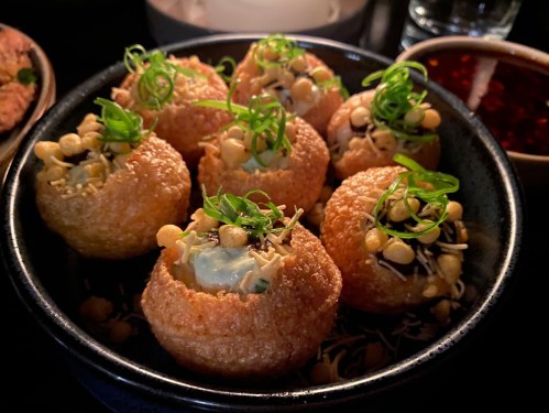 A bowl of crispy puris filled with green chutney, topped with crunchy noodles and garnished with green onions.