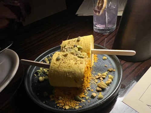 Two ice cream pops on a plate, topped with crushed pistachios and surrounded by a sprinkle of crushed nuts.