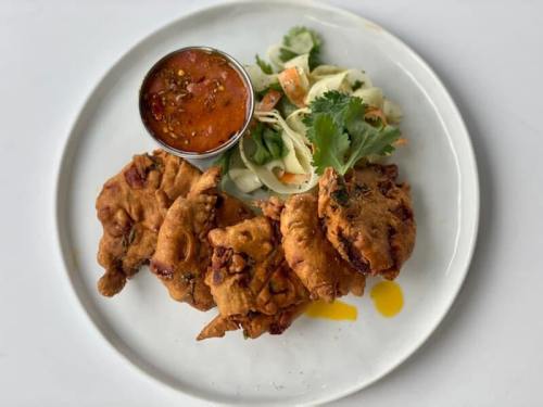 A plate of golden-brown fritters served with a spicy dipping sauce and a side of fresh salad.