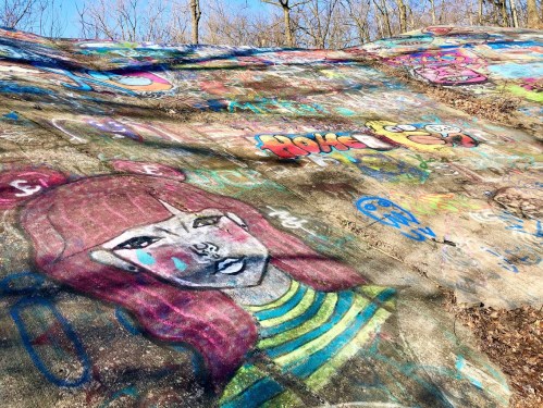 Colorful graffiti on a sloped surface, featuring a large mural of a girl with pink hair and various vibrant designs.