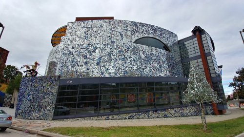 A modern building with a colorful, abstract exterior design and large glass windows, surrounded by greenery.