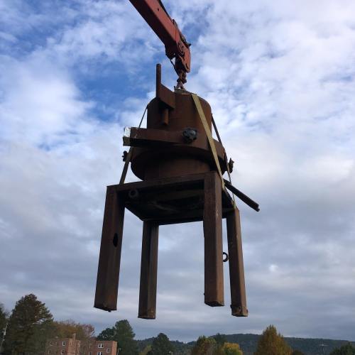 A crane lifting a large industrial container against a cloudy sky.