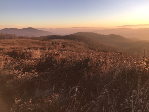 A serene mountain landscape at sunset, with rolling hills and a warm, golden glow illuminating the scene.