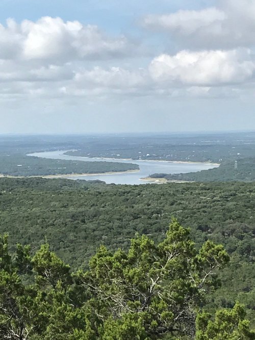 A scenic view of a winding river surrounded by lush green trees under a partly cloudy sky.