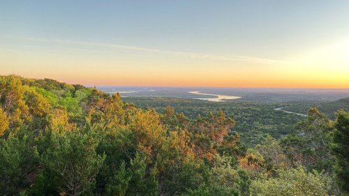 A scenic view of a river winding through lush green hills at sunset, with a colorful sky above.